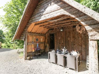 An outdoor covered seating area with a dining table set under a wooden log structure at Pond Farm Woodlands in Ugthorpe