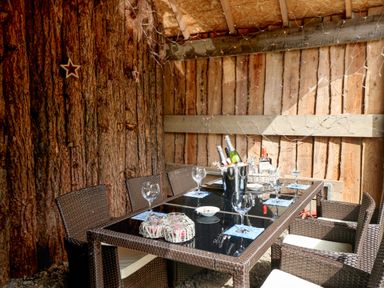 An outdoor dining area with a glass table set with wine glasses bottles and wicker chairs at Pond Farm Woodlands in Ugthorpe