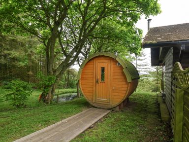 A wooden barrel-shaped sauna next to a house in a garden at Pond Farm Woodlands in Ugthorpe
