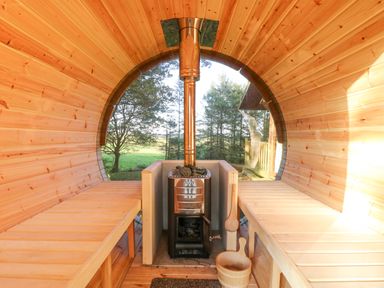 Interior of a wooden barrel sauna with a stove in the center and benches on both sides at Pond Farm Woodlands in Ugthorpe