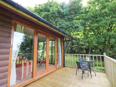 A wooden deck with a small table and two chairs outside a cabin at Pond Farm Woodlands in Ugthorpe
