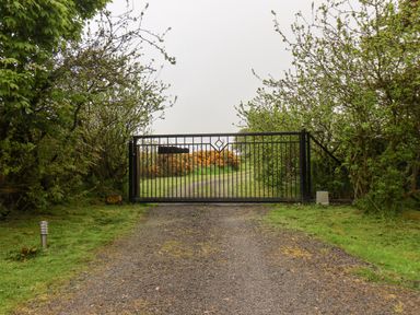 A black metal gate across a gravel driveway surrounded by trees and bushes at Pond Farm Woodlands in Ugthorpe