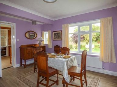 A dining room with a wooden table and chairs near large windows at Glenhaven in Sweffling near Snape