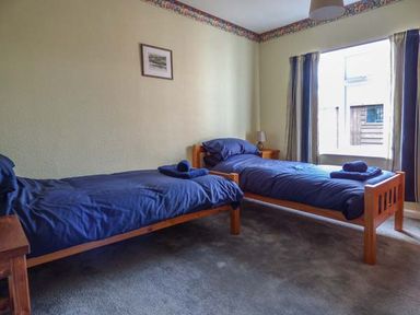 A bedroom with two single wooden beds with blue bedding and towels and a window with curtains at Glenhaven in Sweffling near Snape