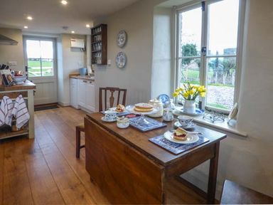 A kitchen with a wooden table set for tea and flowers on the windowsill at Rose Cottage in Welsh Newton