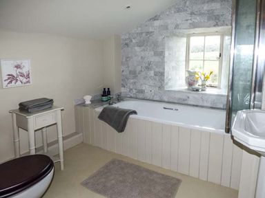 A bathroom with a bathtub under a window and a small table with towels at Rose Cottage in Welsh Newton