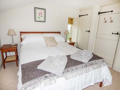 A bedroom with a double bed two bedside tables with lamps towels on bed and two doors at Rose Cottage in Welsh Newton