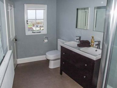 A bathroom with a double sink vanity toilet window and radiator at Woodland Cottage in Malvern