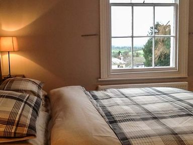 A bedroom with a bed near a window and a lit lamp on a bedside table at Woodland Cottage in Malvern