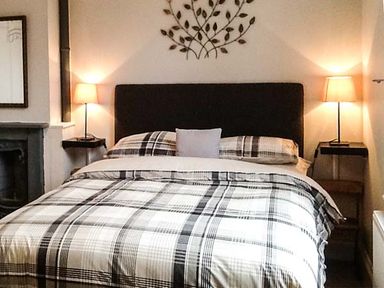 A bedroom with a double bed a plaid bedspread two bedside tables with lamps and a wall decoration above the headboard at Woodland Cottage in Malvern