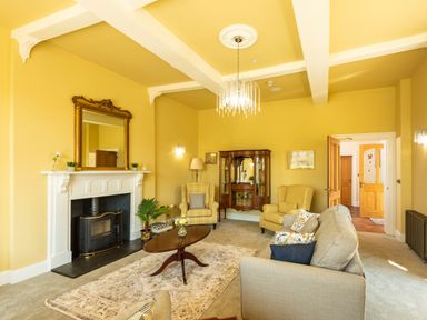 A living room with yellow walls a fireplace two armchairs a sofa a wooden coffee table and a cabinet at Old Rectory House Caersws