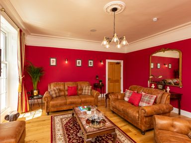 A living room with red walls brown leather sofas a wooden coffee table and a large mirror at Old Rectory House Caersws