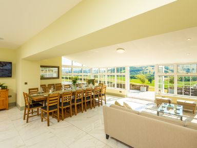 A dining area with a long wooden table and chairs next to a living room with a beige sofa and glass coffee table at Old Rectory House Caersws