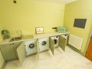 A laundry room with three washing machines under counter next to a sink and a laundry basket at Old Rectory House Caersws