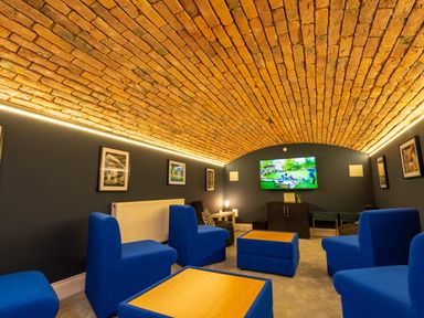 A room with a curved brick ceiling blue chairs wooden tables a television and framed pictures on the walls at Old Rectory House in Caersws