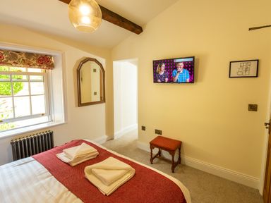 A bedroom with a bed with folded towels a window with floral blind a wall mirror a small stool and a wall mounted tv at Old Rectory House in Caersws