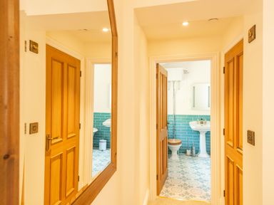 A hallway with wooden doors leading to a bathroom with blue tiled walls a pedestal sink and a toilet at Old Rectory House in Caersws