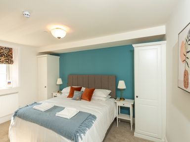 A bedroom with a double bed, two white bedside tables with lamps, two white wardrobes and a window with a patterned roman blind at Old Rectory House in Caersws