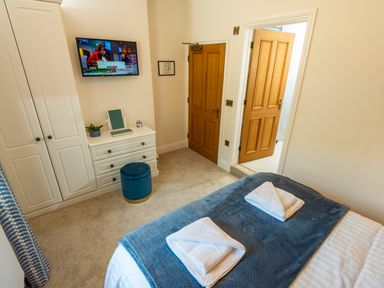 A bedroom with a bed and folded towels a dresser with a stool and a wall mounted tv at Old Rectory House in Caersws