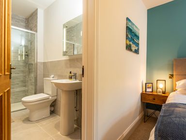 A bathroom with a toilet, sink, and shower next to a bedroom with a bed, nightstand, lamp, and painting at Old Rectory House in Caersws