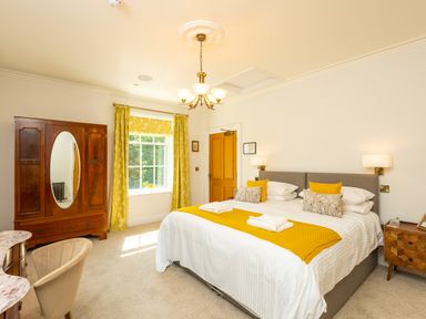 A bedroom with a large bed yellow throw pillows yellow curtains a wooden wardrobe and a wooden nightstand at Old Rectory House in Caersws