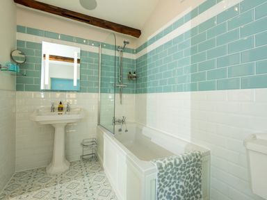 A bathroom with a bathtub with showerhead a pedestal sink and patterned floor tiles at Old Rectory House Caersws