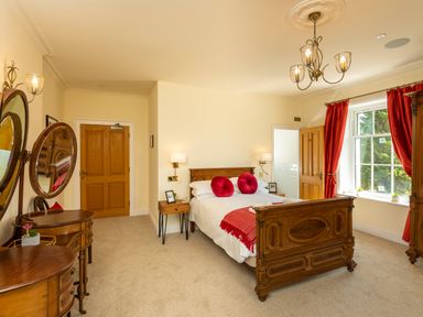 A bedroom with a wooden bed and red pillows red curtains and wooden furniture at Old Rectory House in Caersws