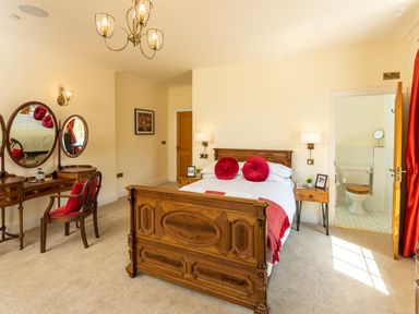 A bedroom with a wooden bed and vanity table next to an ensuite bathroom at Old Rectory House in Caersws