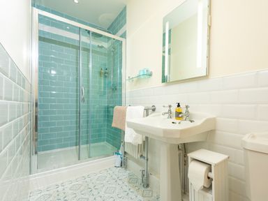 A bathroom with a glass shower enclosure, white pedestal sink, wall-mounted mirror, and patterned floor tiles at Old Rectory House in Caersws