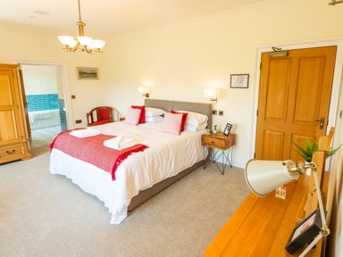 A bedroom with a double bed with red and pink pillows wooden furniture and a door to a bathroom at Old Rectory House Caersws