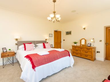 A bedroom with a large bed red pillows wooden dresser and side table at Old Rectory House in Caersws