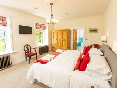 A bedroom with a bed red pillows wooden wardrobe chair and windows at Old Rectory House in Caersws