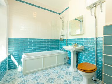 A bathroom with blue and white tiles a bathtub a pedestal sink a mirror and a toilet with a wooden seat at Old Rectory House in Caersws