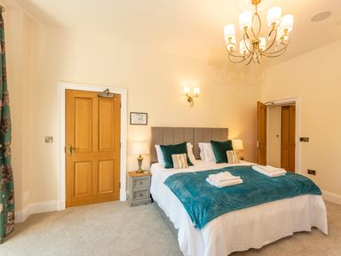 A bedroom with a double bed bedside tables lamps wooden doors and teal accents at Old Rectory House in Caersws