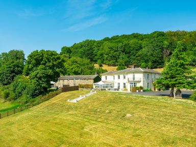 A large white house and a stone building on a grassy hill with trees in the background at Old Rectory House in Caersws