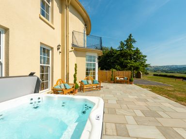 An outdoor patio with a hot tub wooden benches with cushions and a view of trees and fields at Old Rectory House in Caersws