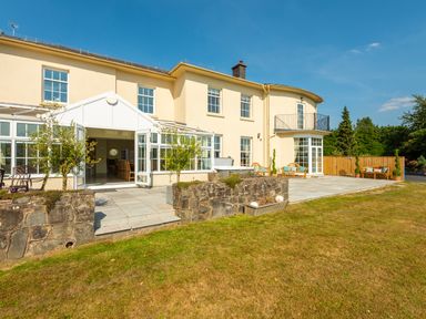 A large cream colored house with multiple windows and a conservatory opening to a stone patio and garden at Old Rectory House in Caersws