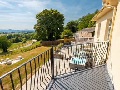 A balcony overlooking a garden with a hot tub and seating area at Old Rectory House in Caersws