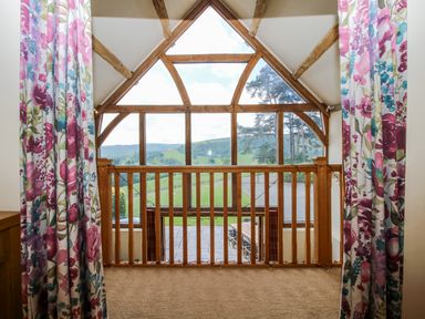 A balcony with wooden railing and curtains at The Hayloft in Bleddfa near Knighton