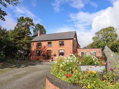 A brick house with a driveway and flower bed in front at Ty Newydd in Llangadfan