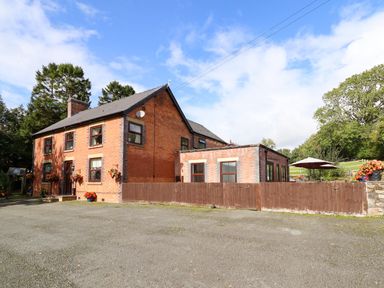 A brick house with a slate roof and brown wooden fence in front with trees and patio umbrellas at Ty Newydd in Llangadfan