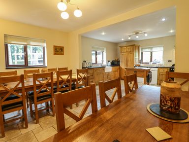 A dining area with wooden tables and chairs adjacent to a kitchen with wooden cabinets and appliances at Ty Newydd in Llangadfan