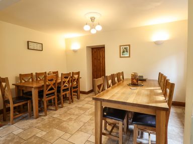 A dining room with two wooden tables and multiple wooden chairs at Ty Newydd in Llangadfan