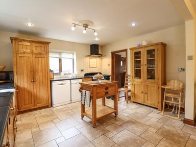 A kitchen with wooden cabinets a central wooden island chair and high chair at Ty Newydd in Llangadfan