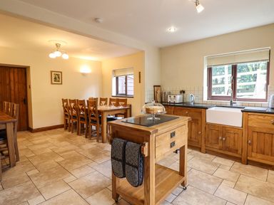 A kitchen with wooden cabinets a sink a wooden dining table with chairs and a wooden island at Ty Newydd in Llangadfan