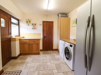 A laundry room with washing machine dryer wooden cabinets and a double-door refrigerator at Ty Newydd in Llangadfan