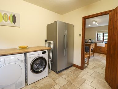 A utility room with a washing machine dryer refrigerator and wooden countertop next to a kitchen at Ty Newydd in Llangadfan