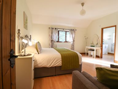 A bedroom with a bed a side table a window with curtains a dressing table and a doorway at Ty Newydd in Llangadfan