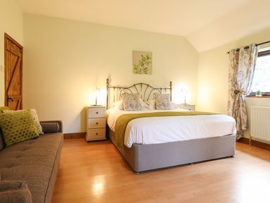 A bedroom with a double bed with bedside tables and lamps a sofa with cushions and a window with patterned curtains at Ty Newydd in Llangadfan