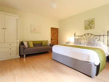 A bedroom with a bed a sofa a wooden door a wardrobe and wall art at Ty Newydd in Llangadfan